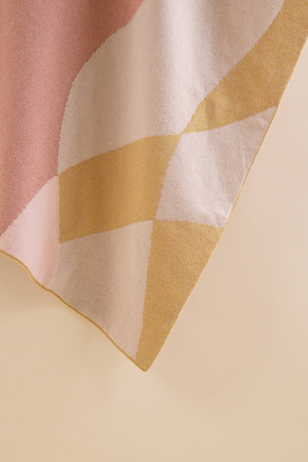 Close-up of a wool knit blanket with geometric pattern in pink, beige, and mustard yellow.