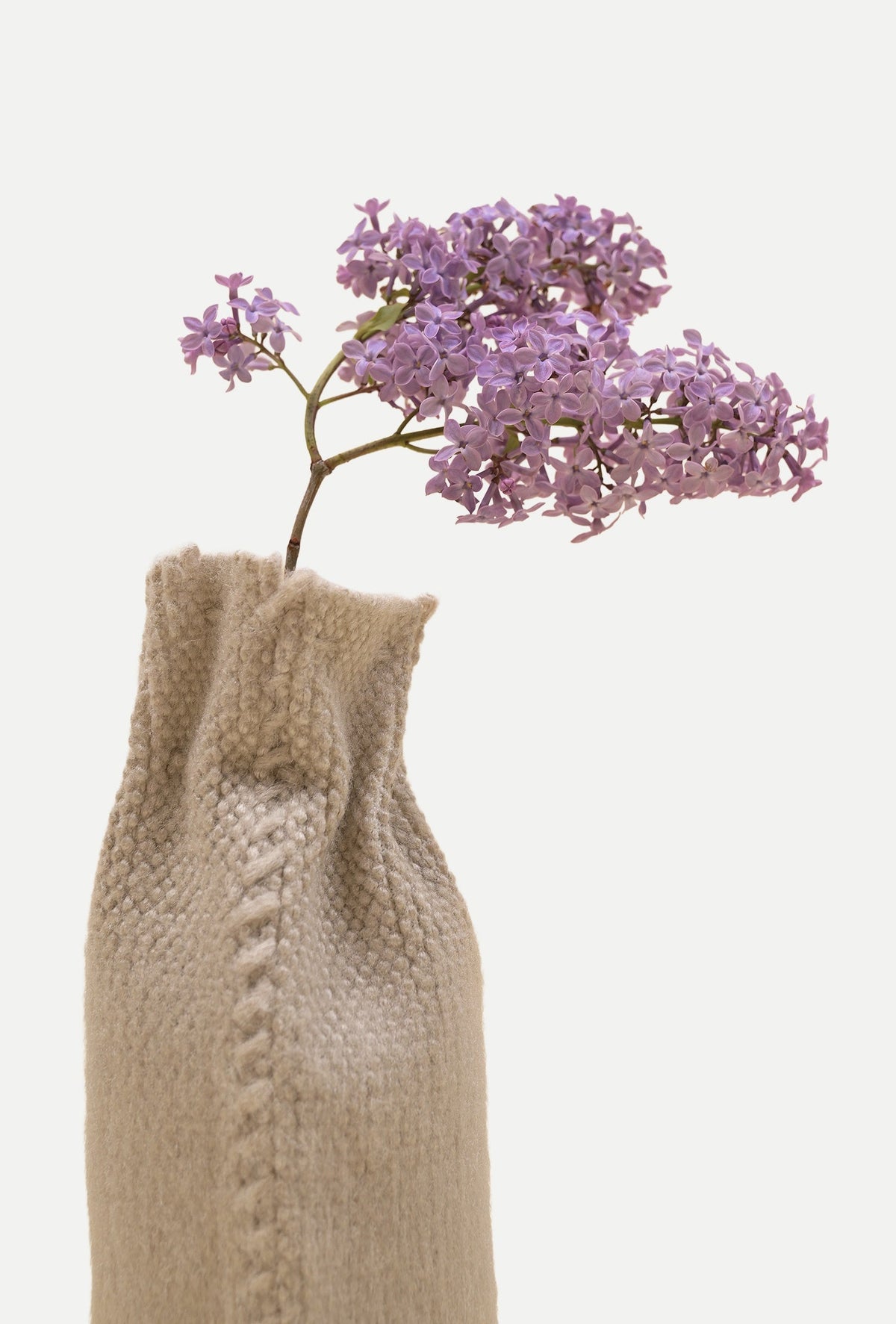 [beige] beige knit textile vase with a leaning spray of purple lilac