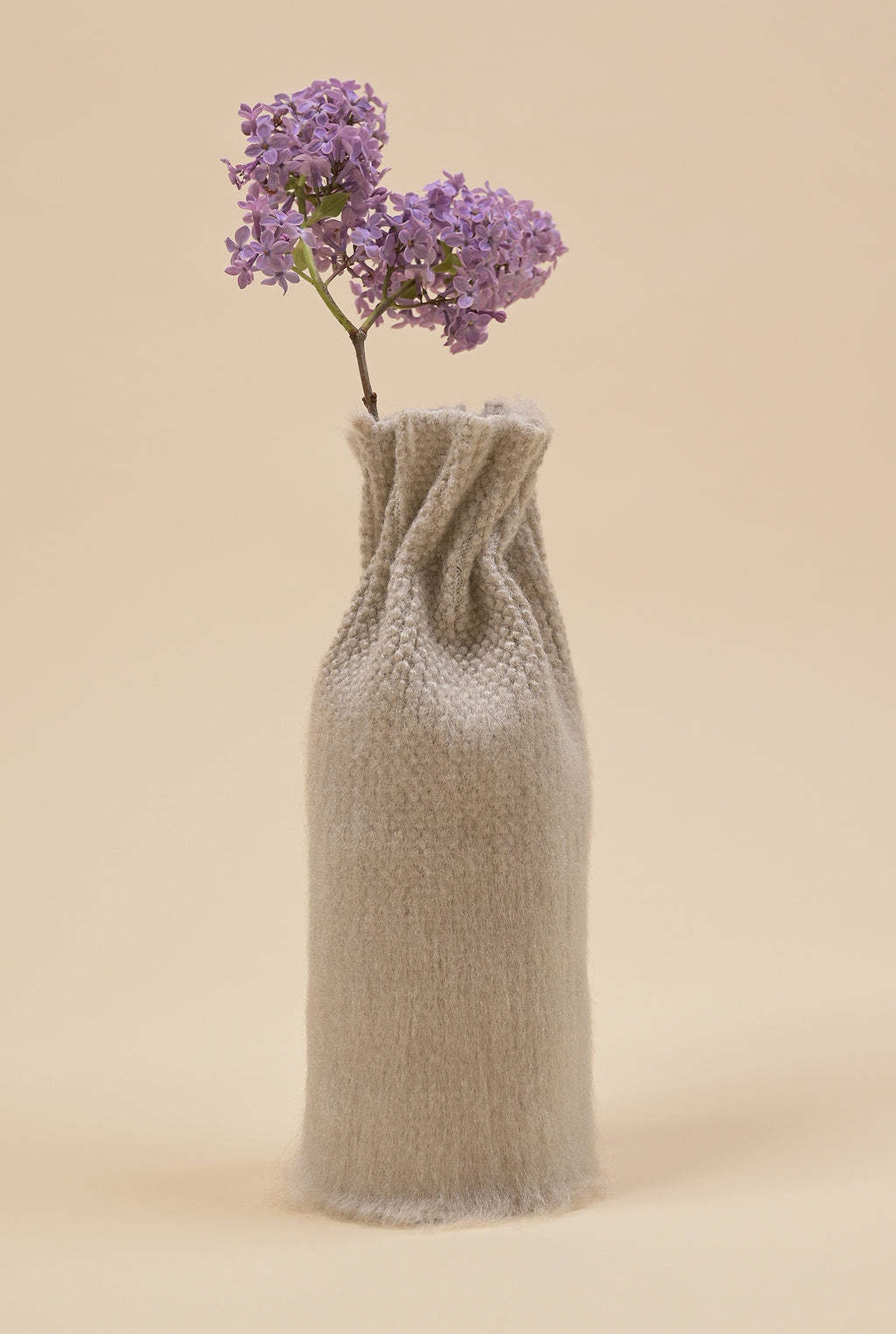 side view of beige knit textile vase in brushed silk and organic cotton with flower and beige background
