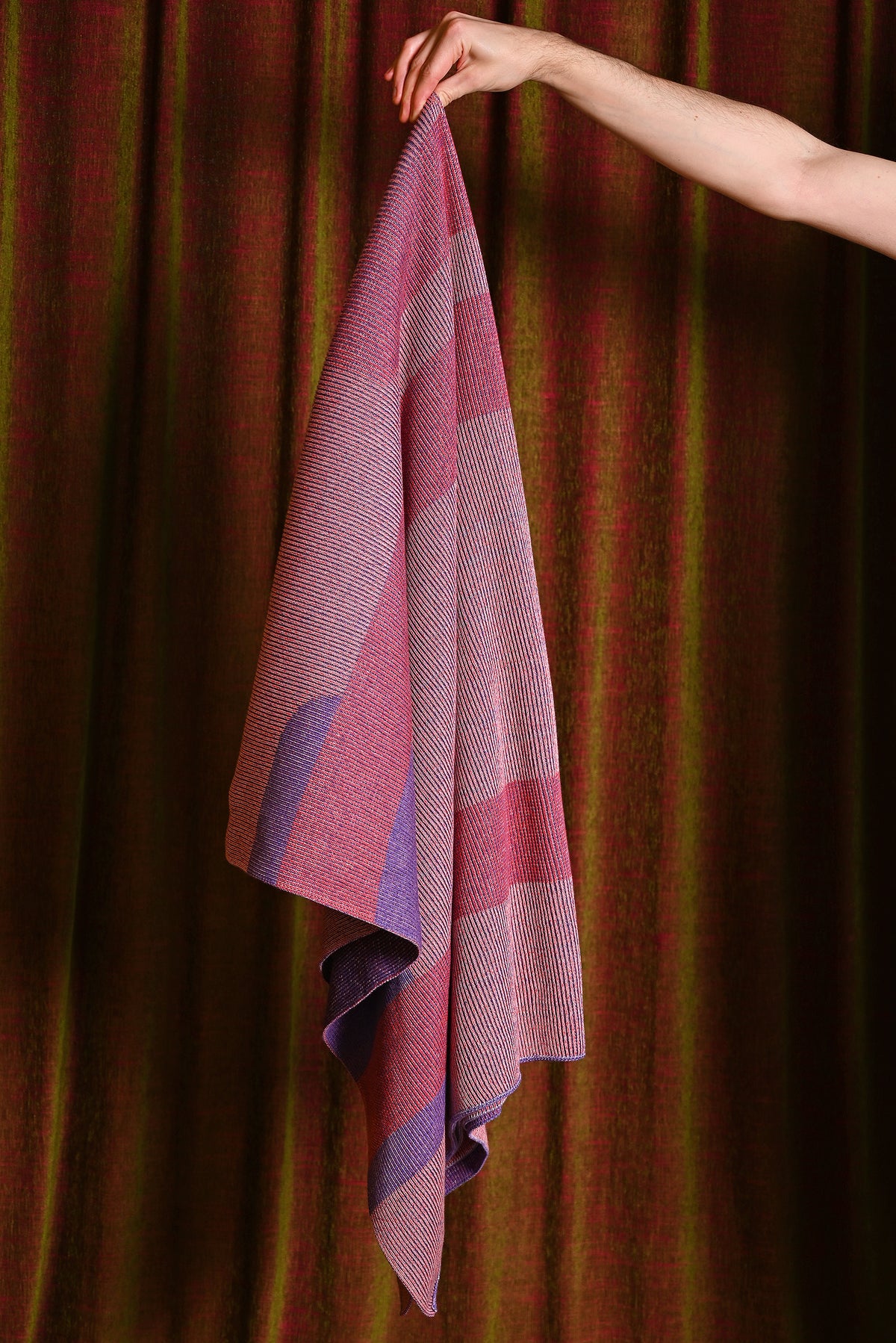 geometric column knit blanket in pink and purple, held up to show drape and texture, wool and organic cotton [pink]