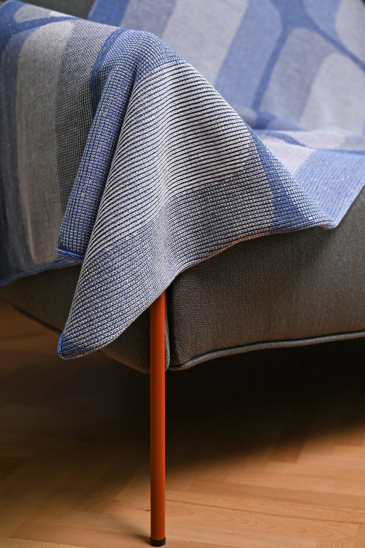 mini-graphic knit blanket in grey and blue, folded corner draped over a sofa arm, wool and organic cotton [grey/blue]