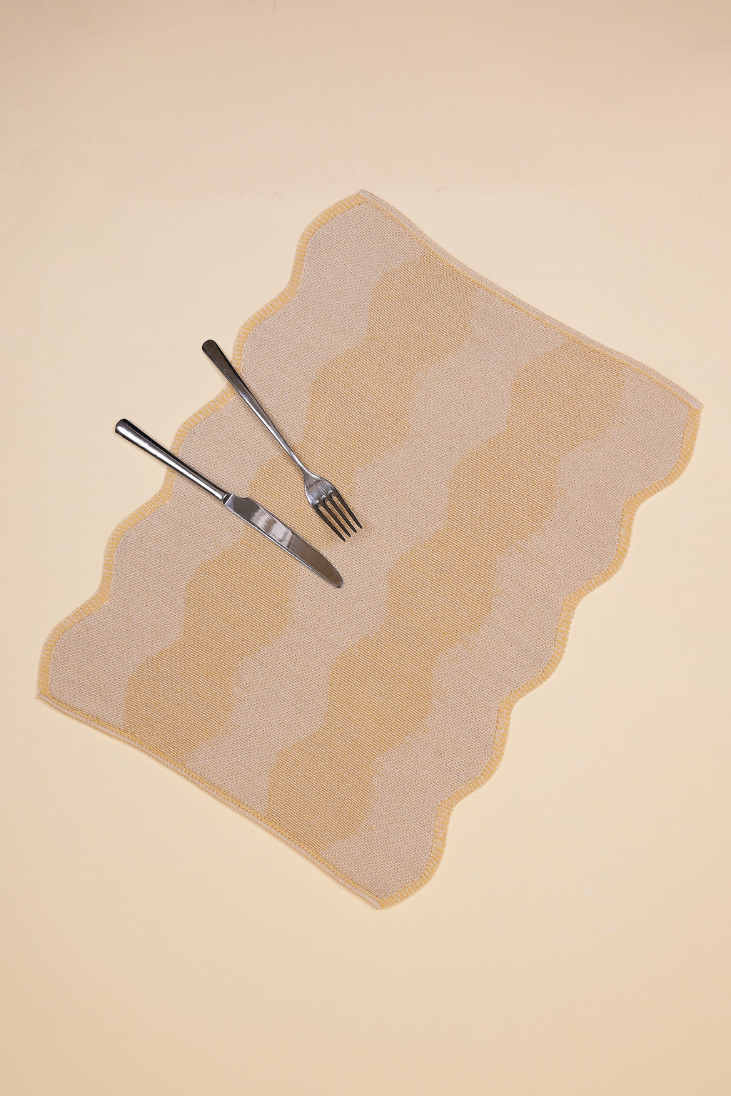 top view of beige and yellow knit organic cotton and hemp table mat with wavy pattern with cutlery 