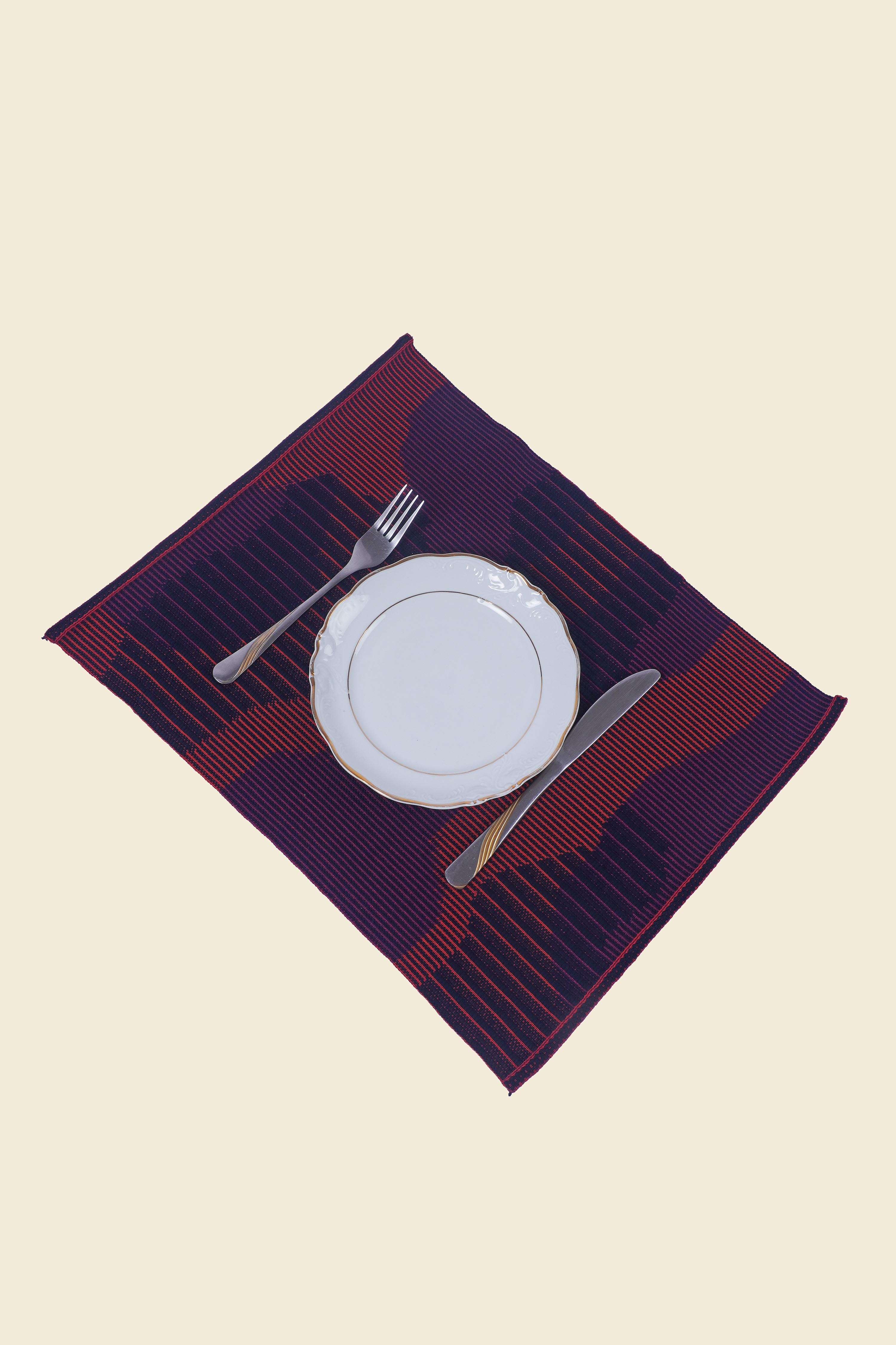 top view of red knit organic cotton table mat with abstract design with plate