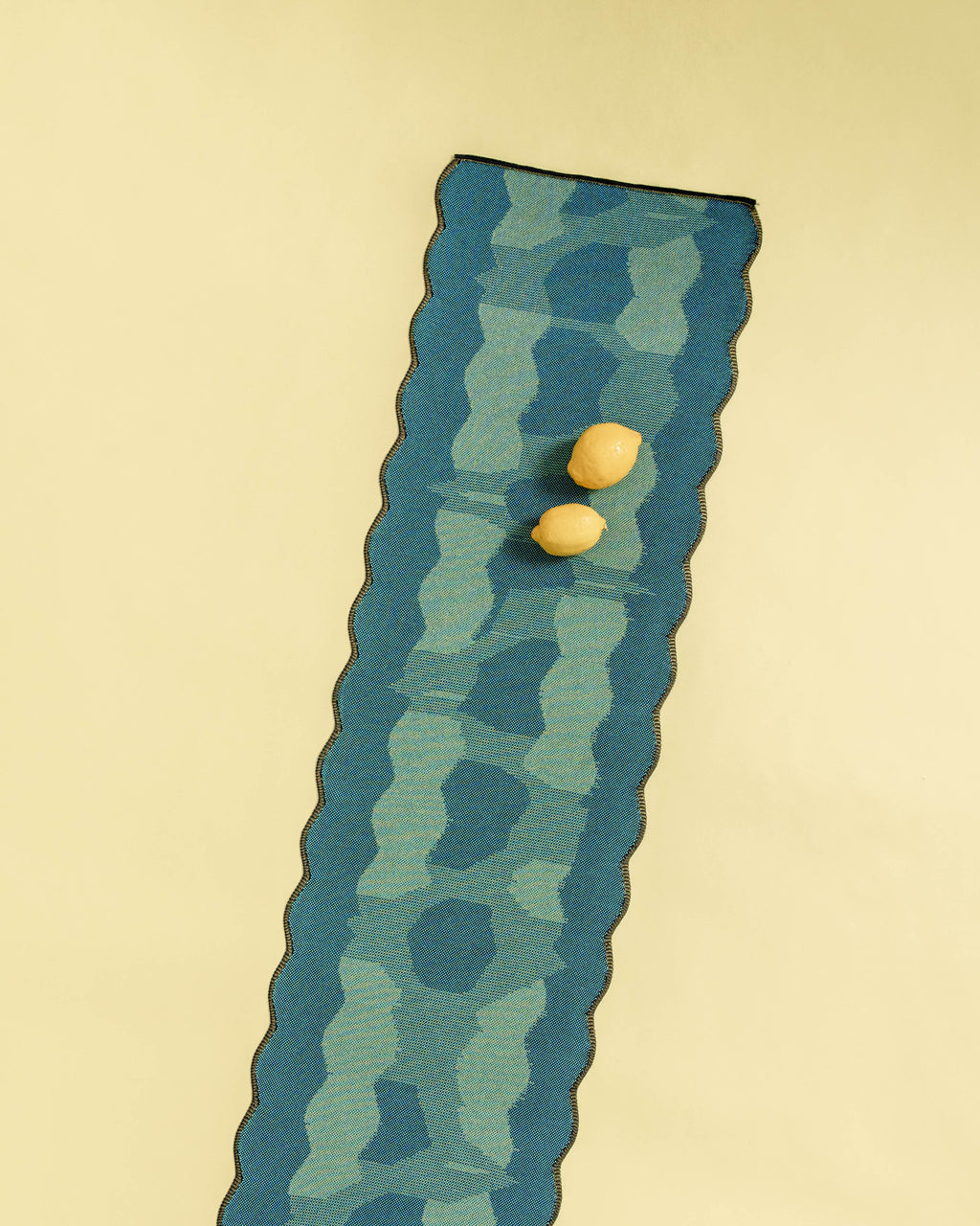 top view of green knit organic cotton and viscose table runner with abstract pattern and wavy edges on yellow background