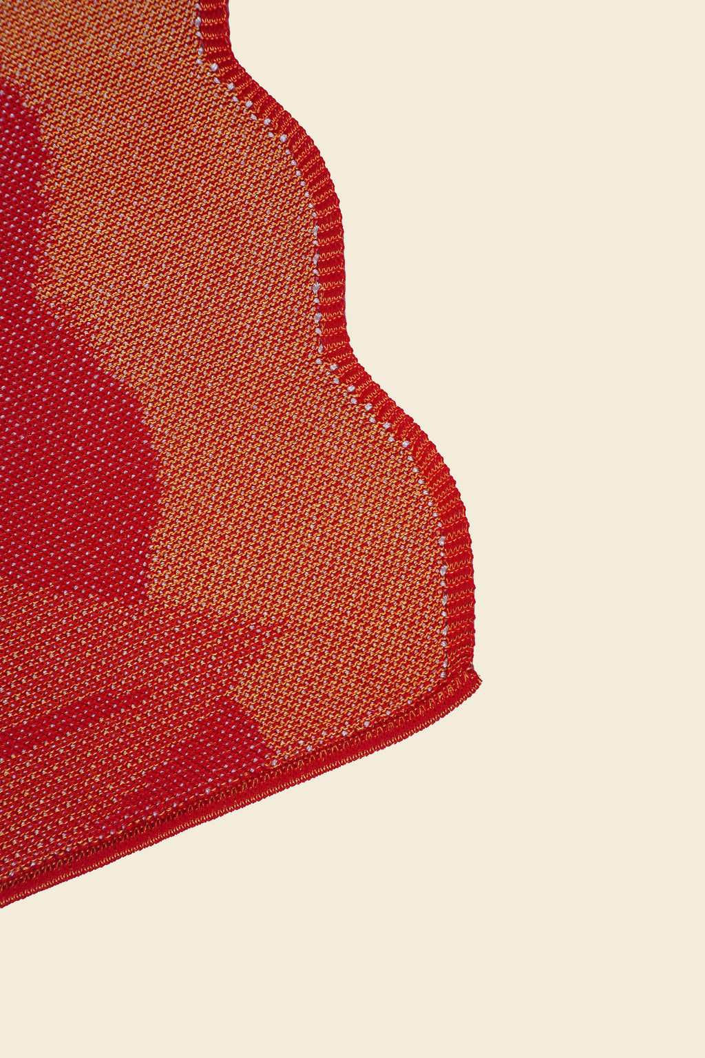 corner of red knit organic cotton and viscose table runner with abstract pattern and wavy edges