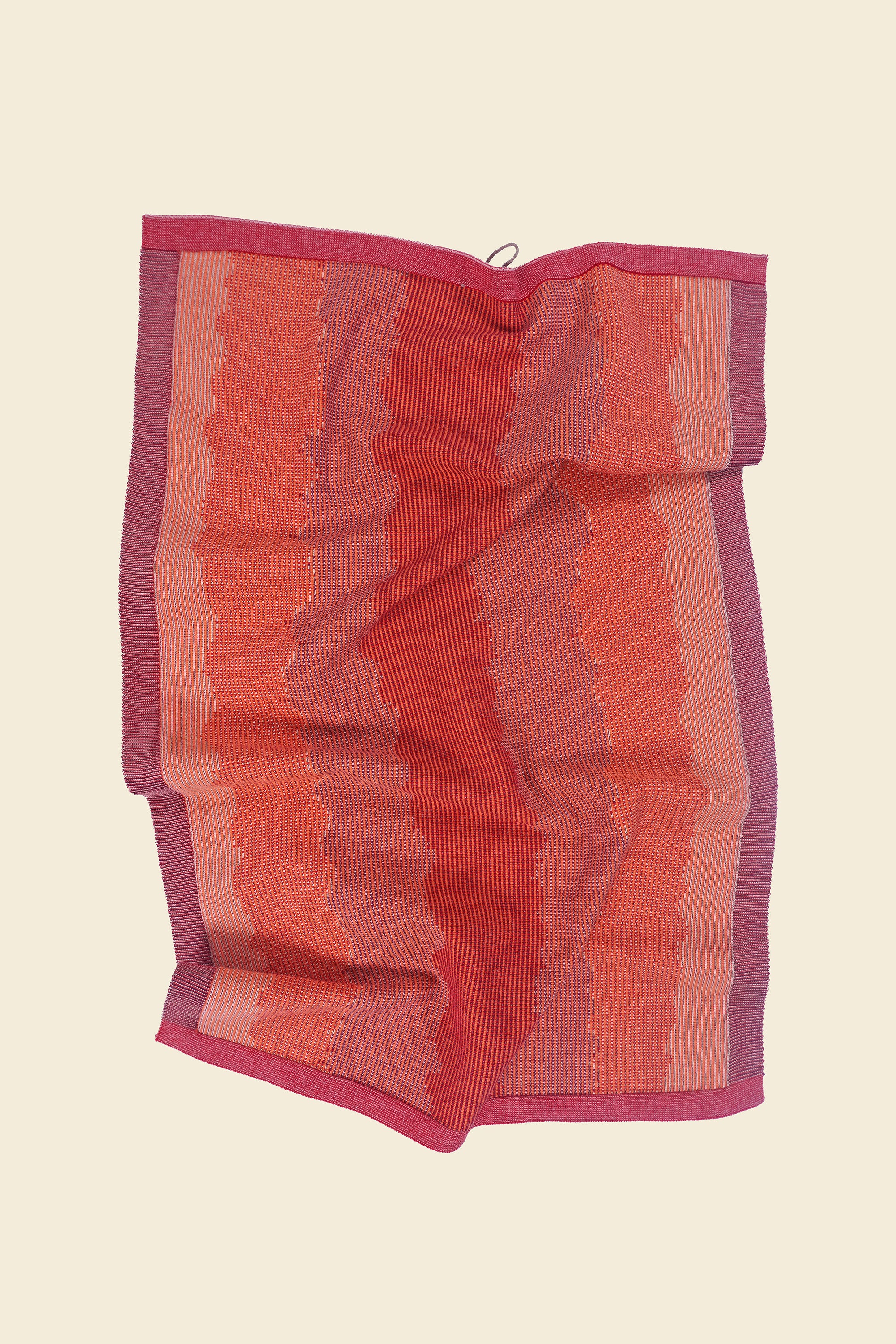 front view of red knit organic cotton kitchen towel with wavy pattern with folds