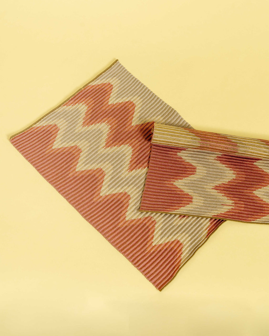 top view of red/gold knit table mat in organic cotton and viscose with wavy pattern with yellow background