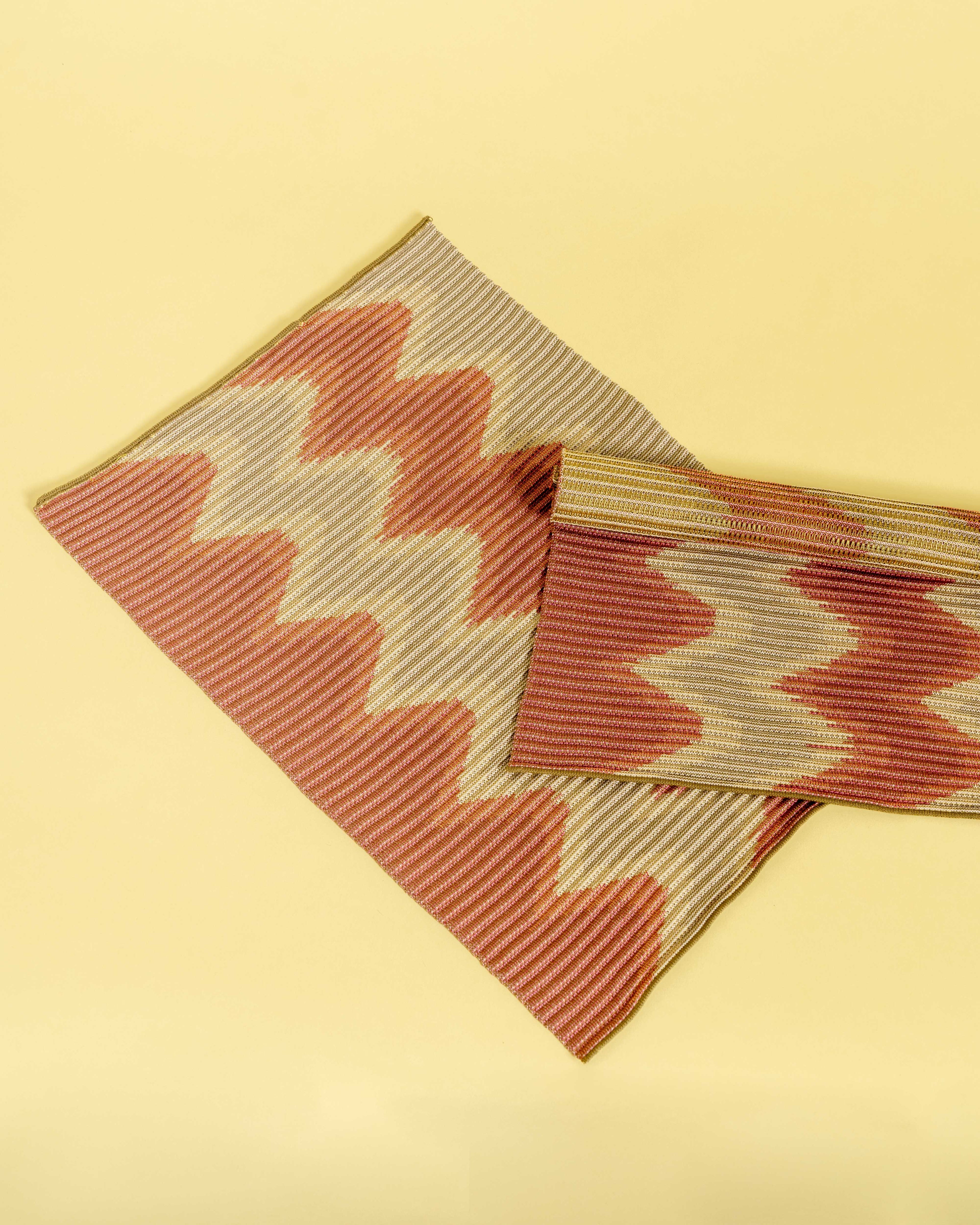 top view of red/gold knit table mat in organic cotton and viscose with wavy pattern with yellow background