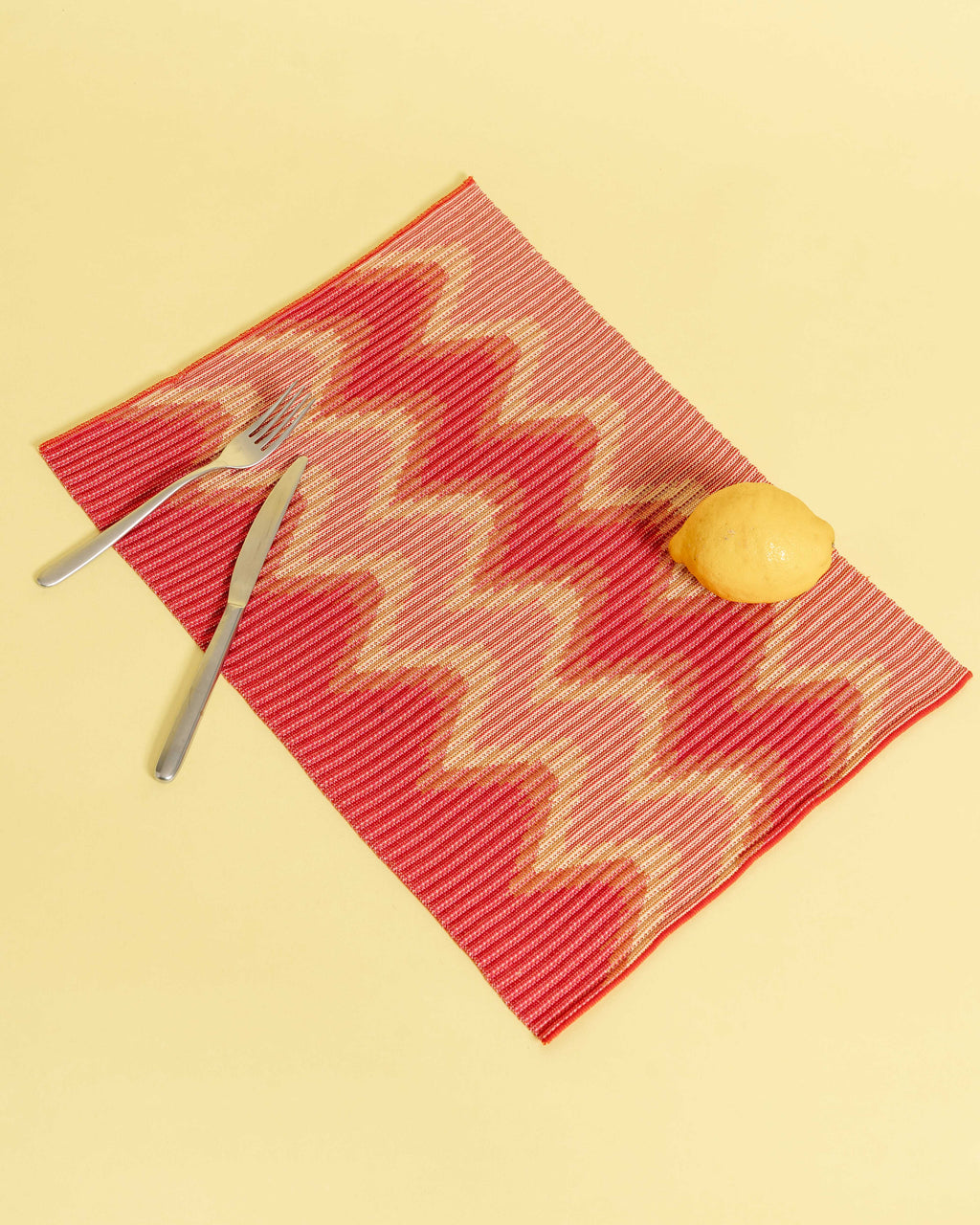 top view of red/yellow knit table mat in organic cotton and viscose with wavy pattern with yellow background
