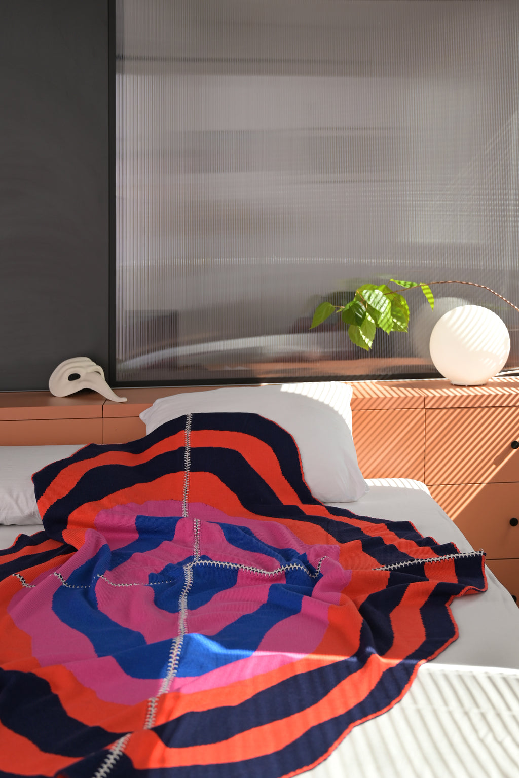dark wavy knit wool blanket on bed with hand-stitched seam in blue, pink, red and navy 