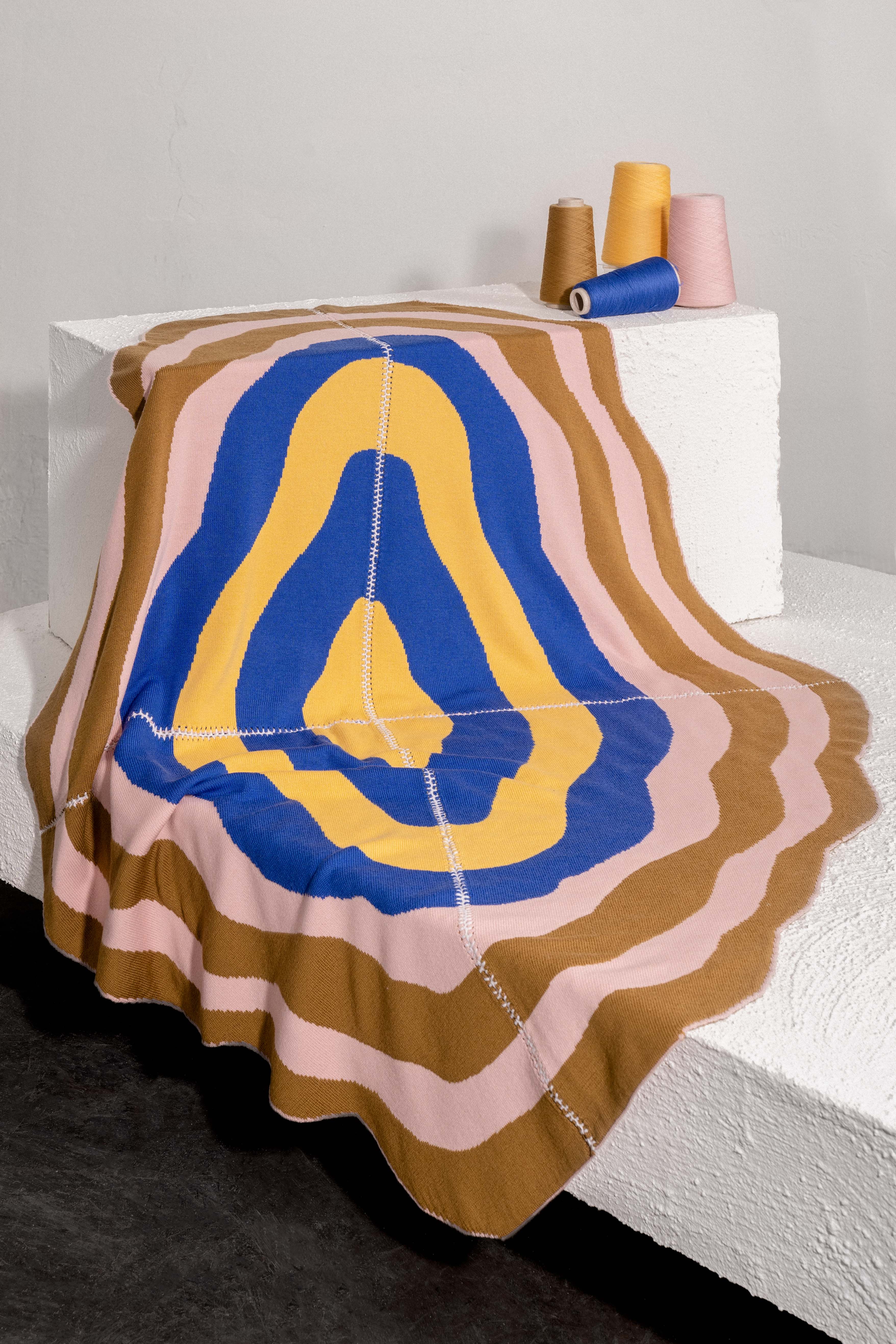 light wavy knit wool blanket in editorial setting with hand-stitched seam in blue, yellow, pink, and camel 